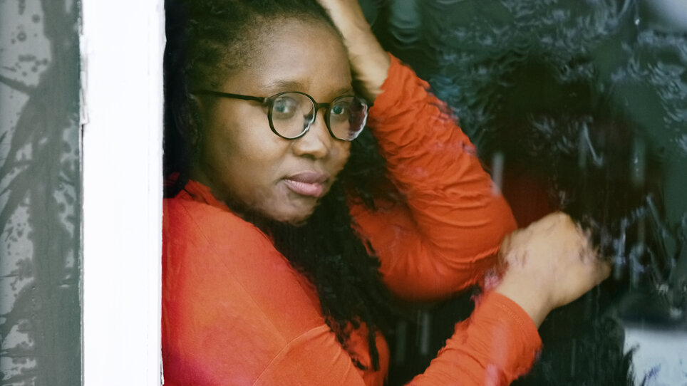 Shot of a sad woman sitting inside home looking through the window glass with rain drops